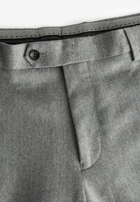 Pantalones gris ajustados con una textura suave, que cuentan con un cierre de botón y un diseño de pliegues frontales limpios. La cinturilla interior presenta un patrón en contraste.