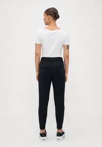 Jogging noir avec une taille élastique à cordon, jambes fuselées et deux poches arrière, associé à un t-shirt blanc ajusté et des baskets noires.