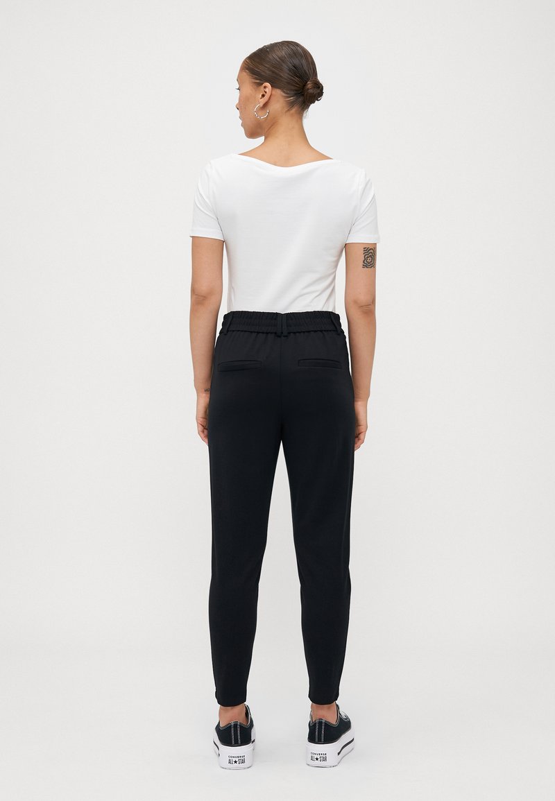 Schwarze Jogginghosen mit einem Kordelzugbund, schmalen Beinen und zwei Gesäßtaschen, kombiniert mit einem eng anliegenden weißen T-Shirt und schwarzen Sneakers.