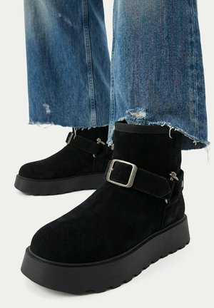 Black suede ankle boots with silver buckle straps worn with frayed hem blue jeans.
