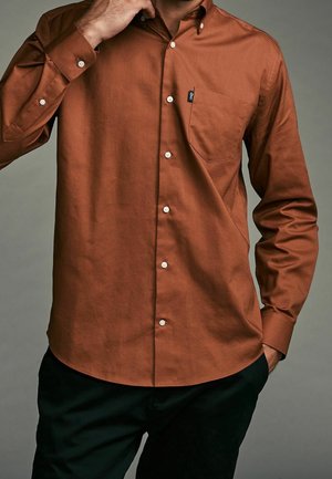 Braunes Hemd mit Knopfleiste, Brusttasche, weißen Knöpfen und glatter Textur. Es hat einen klassischen Kragen und lange Ärmel.