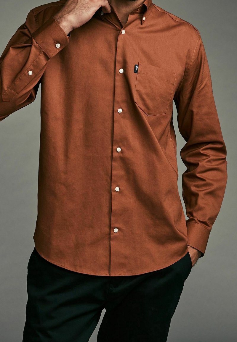 Braunes Hemd mit Knopfleiste, Brusttasche, weißen Knöpfen und glatter Textur. Es hat einen klassischen Kragen und lange Ärmel.