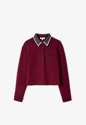 Chemise bordeaux courte avec un avant à boutons, col gris foncé contrastant, piping blanc et une poche à rabat sur le côté gauche.
