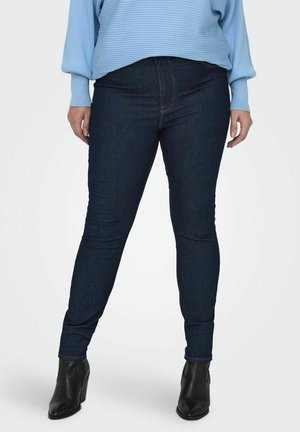Tmavě modré skinny džíny z denimu, s klasickým pasem a jemnými švy, doplněné černými kotníkovými botami.