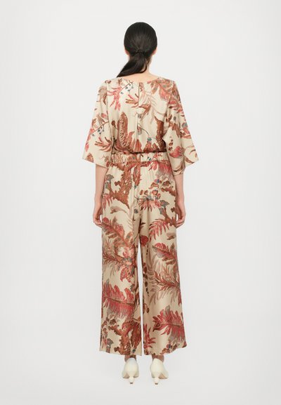 Beige jumpsuit med et blomsterprint i rød og blå. Har brede ærmer, elastisk talje og løse, svævende bukser.
