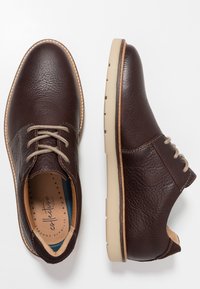 Chaussures en cuir marron avec une finition texturée, un design à lacets, une semelle beige et des coutures contrastées. L'intérieur comprend une semelle intérieure rembourrée.