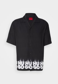 Chemise noire à manches courtes boutonnée avec col camp et motif flamme blanc épelant "HUGO" le long de l'ourlet inférieur.