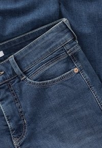 Jeans de color azul oscuro en material vaquero, con una cinturilla estándar, bolsillos laterales y un acento de remache de color cobre en el bolsillo delantero.