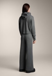 Hanorac gri, scurtat, cu glugă și pantaloni largi asortați, confecționați dintr-un material moale, cu manșete striate și croială lejeră.