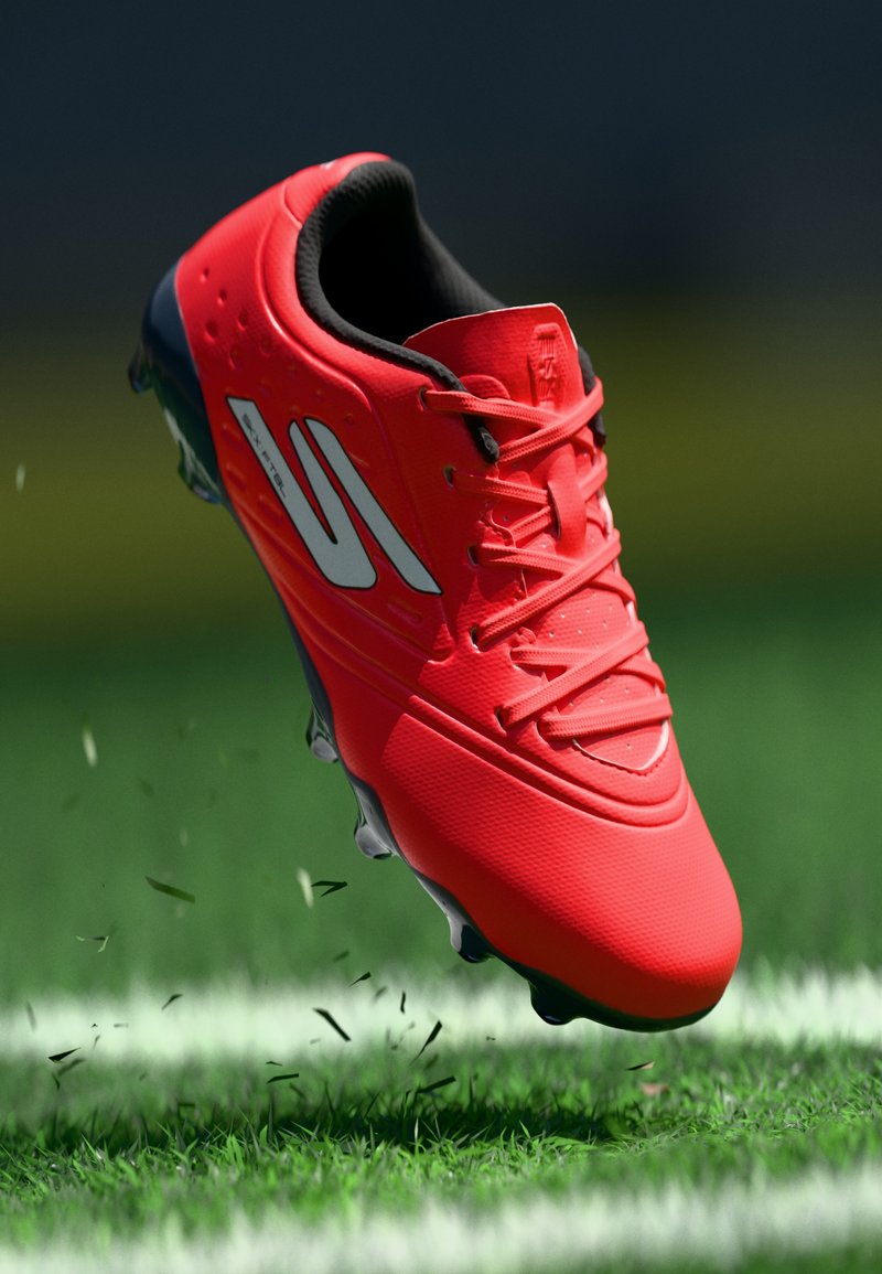 Φωτεινό κόκκινο ποδοσφαιρικό παπούτσι με μαύρη σόλα και λευκό λογότυπο, στον αέρα πάνω από χλοοτάπητα κοντά σε λευκή γραμμή, με κομμένα χόρτα να πετούν γύρω.