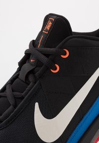 Nike trainingschoenen hebben een zwarte bovenkant met mesh en textuuraccenten, heldere oranje veterogen en een prominente witte Swoosh-logo.