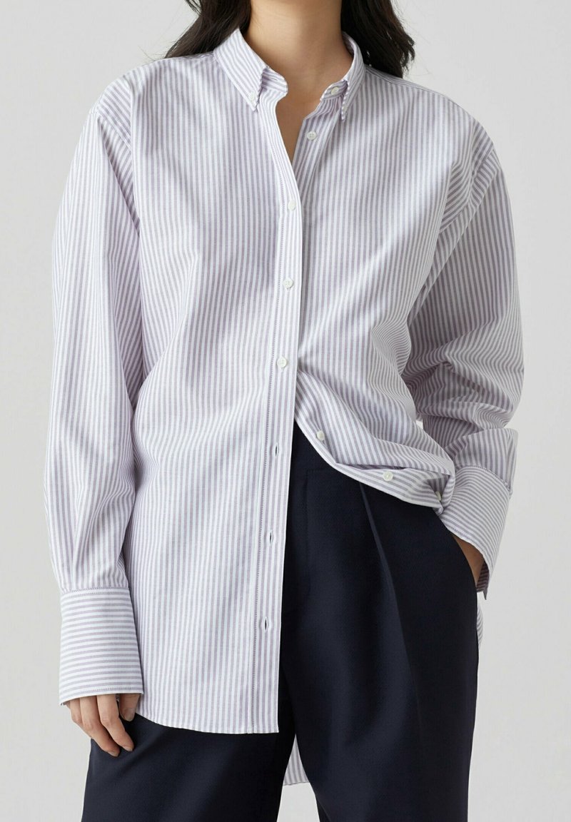 Camicia a righe con bottoni in lilla chiaro e bianco, dotata di colletto, maniche lunghe e una vestibilità comoda. Il tessuto sembra liscio e leggero.