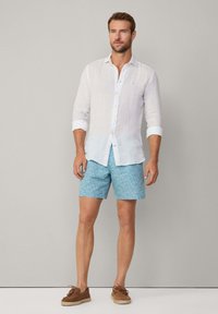 Camicia bianca in lino con maniche lunghe, pantaloni corti a righe blu chiaro e scarpe stringate marroni. Design minimalista e tessuto traspirante.