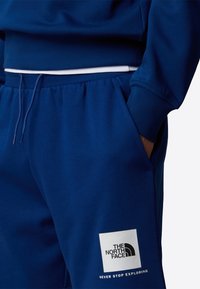 Sudadera azul marino con puños y cintura de canalé, que presenta un parche de logo en el lado izquierdo. El material parece suave y resistente.