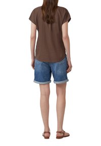 Haut marron à manches courtes avec un ourlet arrondi, associé à un short en denim bleu retroussé aux poignets. Les sandales comportent une sangle et un charme décoratif.