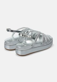 Zilveren platform sandalen met kruisgewoven banden en een metallic glanzende afwerking. Platte rubberen zool, enkelband met gesp.