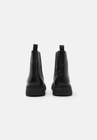 Bottes chevilles en cuir noir avec une finition texturée, semelle en caoutchouc épaisse et languettes à l'arrière. Logo "JOOP!" embossé sur la semelle.