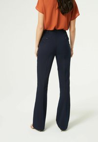 Navyblauwe flared broek met een gladde textuur, met een middenhoog taille en twee achterzakken, gecombineerd met een oranje blouse.