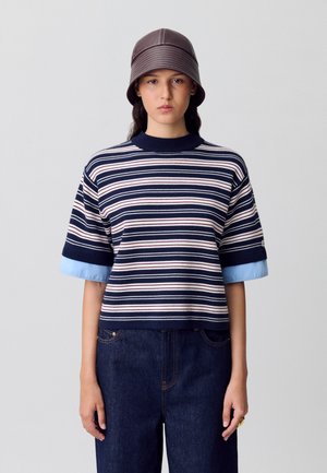 Pull en tricot rayé bleu marine et crème à manches courtes, avec des poignets bleu clair. Assorti à un pantalon en denim foncé.