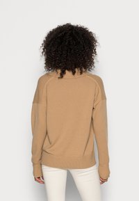 Pull en maille couleur fauve avec un col montant, des épaules tombantes et des poignets côtelés. Texture douce, coupe décontractée, sans motifs visibles.