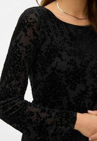 Melnas samta kleitas ar ziedu rakstu, garām piedurknēm un laivu formas kakla izgriezumu. Iespējojusi teksturētu audumu un gludu, elegantu dizainu.