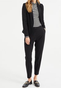 Svart skräddarsydd blazer över en svart- och vitrandig polotröja, kombinerad med smala svarta byxor och loafers med guldkedjedetalj.