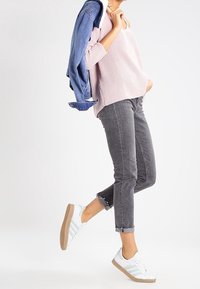 Pull en maille côtelée rose clair, jeans gris slim avec ourlets effilochés, baskets blanches à rayures bleu clair, et une veste en jean posée sur l'épaule.