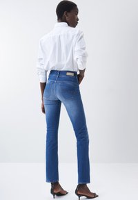 Vaqueros de denim azul ajustados con un lavado oscuro, ligero desgaste en los muslos, diseño de cinco bolsillos y una etiqueta en la cintura trasera.