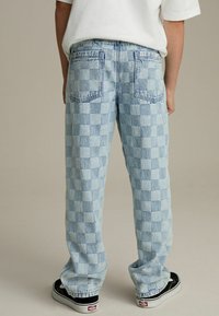 Lichtblauwe geblokte denim broek met een relaxte pasvorm, voorzien van achterzakken en contrasterende stiksels, gecombineerd met zwarte sneakers.