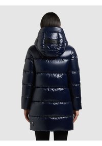 Tumši zila pūdera jaka ar spīdīgu apdari, kas ir aprīkota ar augstu kapuci, horizontālām šūtiem daļām un logotipa detaļu uz muguras.