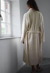 Peignoir couleur crème avec un motif texturé du mot « self ». Ceinture à la taille et manches longues. Design minimaliste.