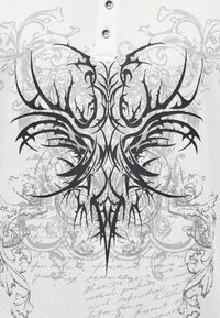 Λευκό υφασμάτινο ύφασμα με μαύρο περίπλοκο γραφικό σχέδιο που παρουσιάζει συμμετρικά στοιχεία και ρέοντα μοτίβα, τονισμένο με ασημένια κουμπιά.