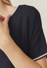 Tumedast sinine soonikuga topp ümmarguse kaelusega ja lühikeste varrukatega, millel on kerge roosa ääre kaeluses ja varruka servades.