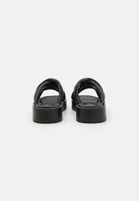 Svarte lærsandaler med rund t�å og polstrede stropper. Har en tykk, solid svart plattformsåle. Minimalistisk design uten dekorasjoner.