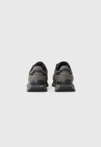 Paire de chaussures de sport gris foncé vue de dos, montrant des semelles texturées et des colliers de talon rembourrés sur un fond clair uni.