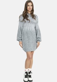 Kobieta ubrana w szarą, wzorzystą dzianinową sukienkę, białe skarpetki z czerwonymi gwiazdkami oraz białe, sznurowane buty na czarnych podeszwach.