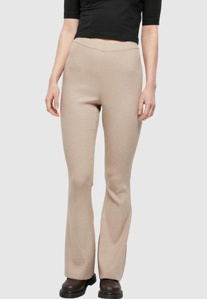 Person wearing beige ribbed knit pants, black cropped top, and dark brown boots on a plain light background.