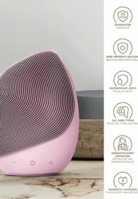 Silikone ansigtsrensningsenhed i pink, der har en tekstureret overflade med små prikker, en let kurve og knapbetjening nederst.