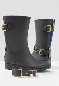 Botas de lluvia de goma negras con hebillas doradas, cremallera azul y suelas texturizadas. Incluye una correa a juego en el suelo.