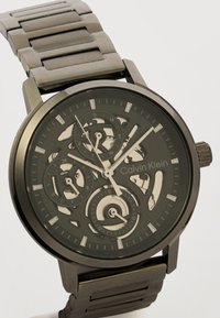 Μεταλλικό ρολόι χειρός Calvin Klein με σκελετό καντράν που δείχνει ώρα, ημέρα, υποκαντράν 24 ωρών και ημερομηνίας με ασημί δείκτες ώρας και δείκτες.