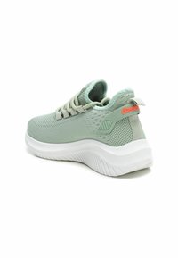 Zapatilla deportiva de color verde claro con una parte superior de malla texturizada, cordones beige y una suela blanca acolchada. Presenta un acento rojo en el talón.