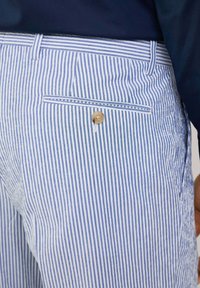 Blue and white striped pants with a back pocket featuring a round brown button. The fabric appears lightweight and has a smooth texture.