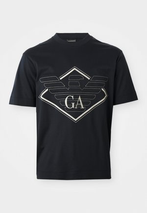 Marineblauwe katoenen t-shirt met een groot zilveren logoontwerp met vleugels en een diamantvorm aan de voorkant. Korte mouwen en ronde hals.