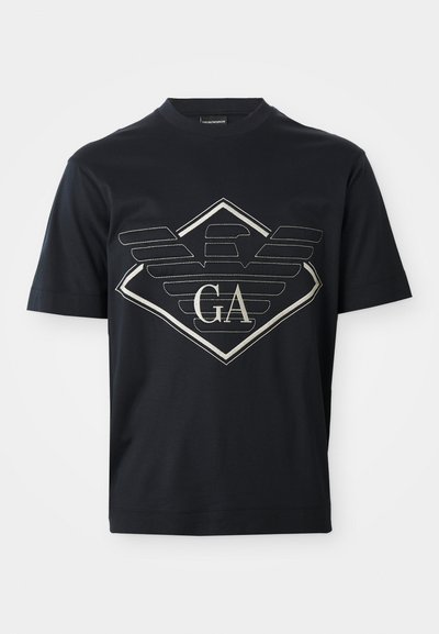 Marineblauwe katoenen t-shirt met een groot zilveren logoontwerp met vleugels en een diamantvorm aan de voorkant. Korte mouwen en ronde hals.