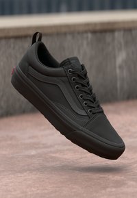 Svart sneaker med en glatt canvas-overdel, snøring, kontrasterende sømmer og en polstret såle. Har en bakre løkke og et ikonisk logo.