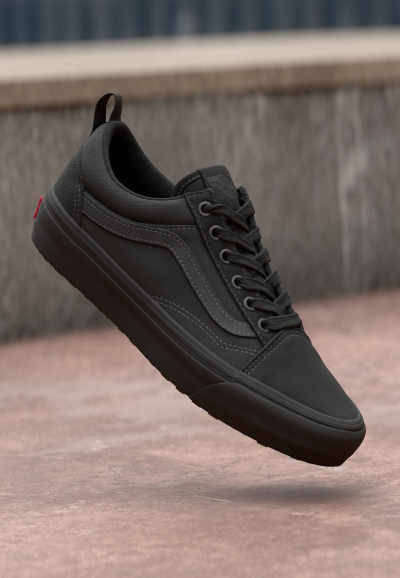 Svart sneaker med en glatt canvas-overdel, snøring, kontrasterende sømmer og en polstret såle. Har en bakre løkke og et ikonisk logo.