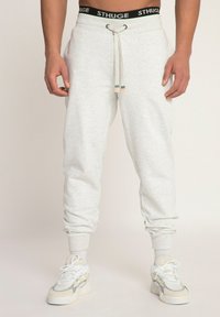 Lichtgrijze joggingbroeken met een elastische tailleband, trekkoord en ribbelmanchetten, gecombineerd met witte en grijze sneakers.