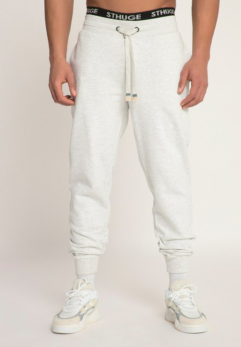 Lichtgrijze joggingbroeken met een elastische tailleband, trekkoord en ribbelmanchetten, gecombineerd met witte en grijze sneakers.