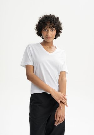 White V-neck t-shirt with short sleeves, made of soft fabric, paired with black pants. Simple, relaxed fit design.