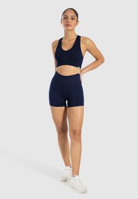 Marinblå sportbehå och högmidjade shorts i ett elastiskt material, med en mjuk yta och minimala sömmar för ökad komfort.